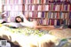 A woman laying on a bed in front of a bookshelf.