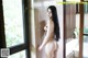 A naked asian woman standing in a bathroom next to a window.