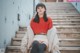 A woman sitting on the steps of a building wearing a red sweater.