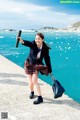 A woman in a school uniform holding a book near the ocean.