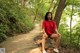 A woman in a red shirt and white shoes sitting on a stone bench.